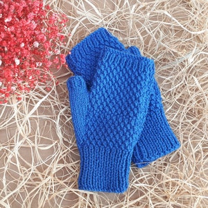 Könnte beinhalten: Ein Paar blaue, gestrickte Fingerhandschuhe mit einem strukturierten Muster. Die Handschuhe sind zusammengefaltet und liegen auf einer braunen Oberfläche.