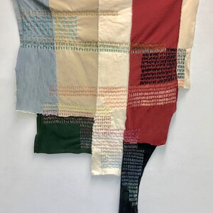 May include: A patchwork quilt made of different colored fabrics, including denim, beige, and red. The quilt is stitched together with colorful thread, creating a geometric pattern.