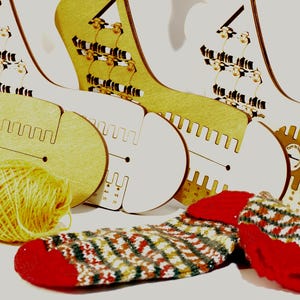May include: Four flat wooden sock blockers with a tan finish, featuring a notched edge and printed numerical scales. A ball of yellow yarn sits to the left, and a partially knitted sock with a red toe and heel and a multi-coloured pattern lies below.