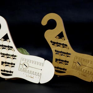 May include: Two flat, foot-shaped wooden sock blockers with a hook at the top. One is white and one is natural light brown wood. Both feature laser-cut patterns, a central slot with a circular dial icon, and the text 5-11 Years printed near the toe.