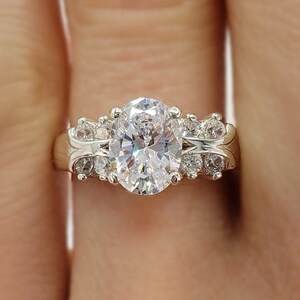 May include: A gold ring with a large oval-shaped center stone and smaller round stones on the band. The ring is on a person's finger.