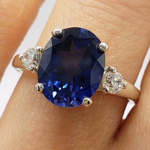 May include: A silver ring with a large oval-shaped blue gemstone and two smaller round white gemstones on the band.