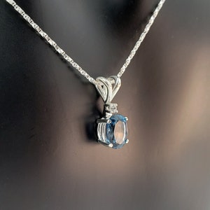 May include: A silver chain necklace with a pendant featuring a blue oval gemstone surrounded by smaller clear gemstones.
