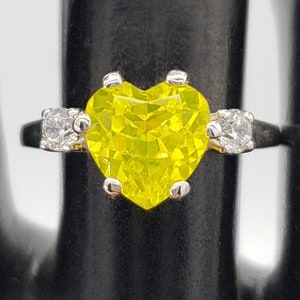 May include: A silver ring featuring a large yellow heart-shaped stone, flanked by two smaller clear stones.