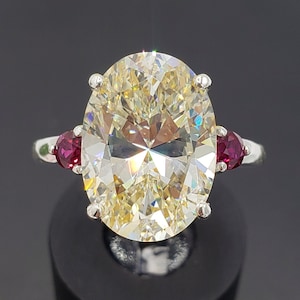 May include: A silver ring with a large oval-shaped clear gemstone and two smaller red gemstones on either side.