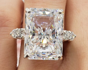 May include: A silver ring with a large, clear, rectangular-shaped gemstone. The gemstone is surrounded by smaller, clear gemstones.