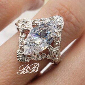 Puede incluir: Un anillo de plata con una piedra grande y transparente de forma marquesa engastada en un dise&ntilde;o de filigrana.