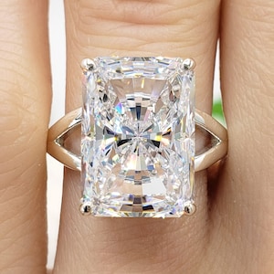 May include: A large, clear, rectangular-shaped diamond ring set in a silver band. The ring is on a finger.