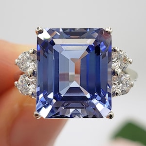 May include: A silver ring with a large, rectangular, blue gemstone surrounded by smaller, round, white gemstones.