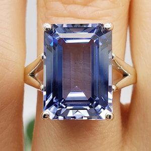 May include: A silver ring with a large, rectangular, blue gemstone. The gemstone is set in a prong setting and has a faceted cut.