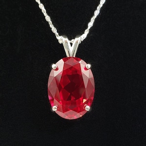 May include: A silver chain necklace with a large oval-shaped red gemstone pendant.