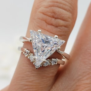 May include: A silver ring featuring a large triangular clear stone and a smaller band of stones set in a v-shape.