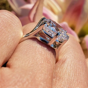 May include: A silver ring with a large, clear, oval-shaped gemstone. The ring is set in a delicate, prong setting.
