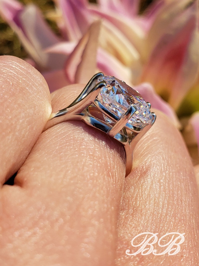 May include: A silver ring with a large, clear, oval-shaped gemstone. The ring is set in a delicate, prong setting.