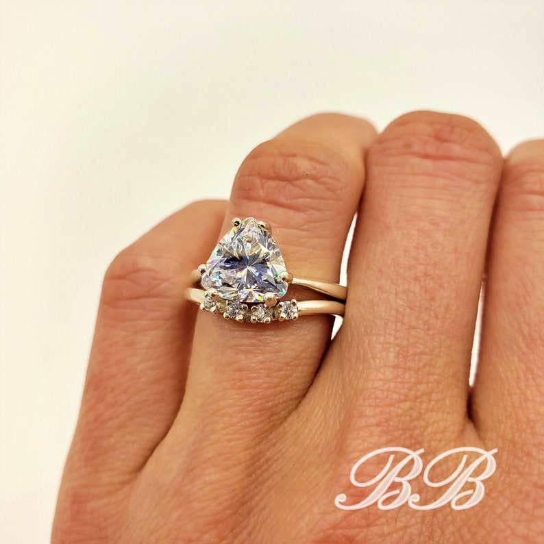 May include: A gold ring set with a large, triangular, clear gemstone. The ring is accented with smaller, clear gemstones on the band.
