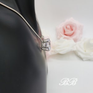 May include: A silver chain necklace with a large, clear cubic zirconia pendant. The pendant is set in a square frame with smaller cubic zirconia stones.