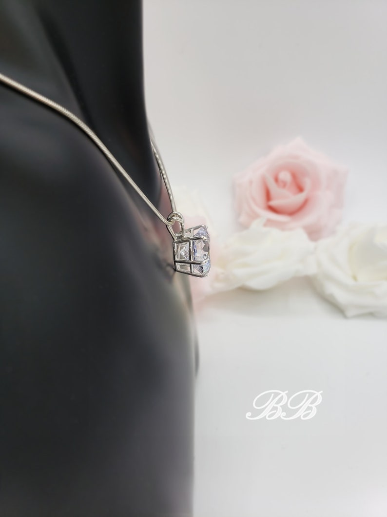 May include: A silver chain necklace with a large, clear cubic zirconia pendant. The pendant is set in a square frame with smaller cubic zirconia stones.