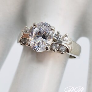 May include: A silver ring with a large oval-shaped clear stone surrounded by smaller clear stones.