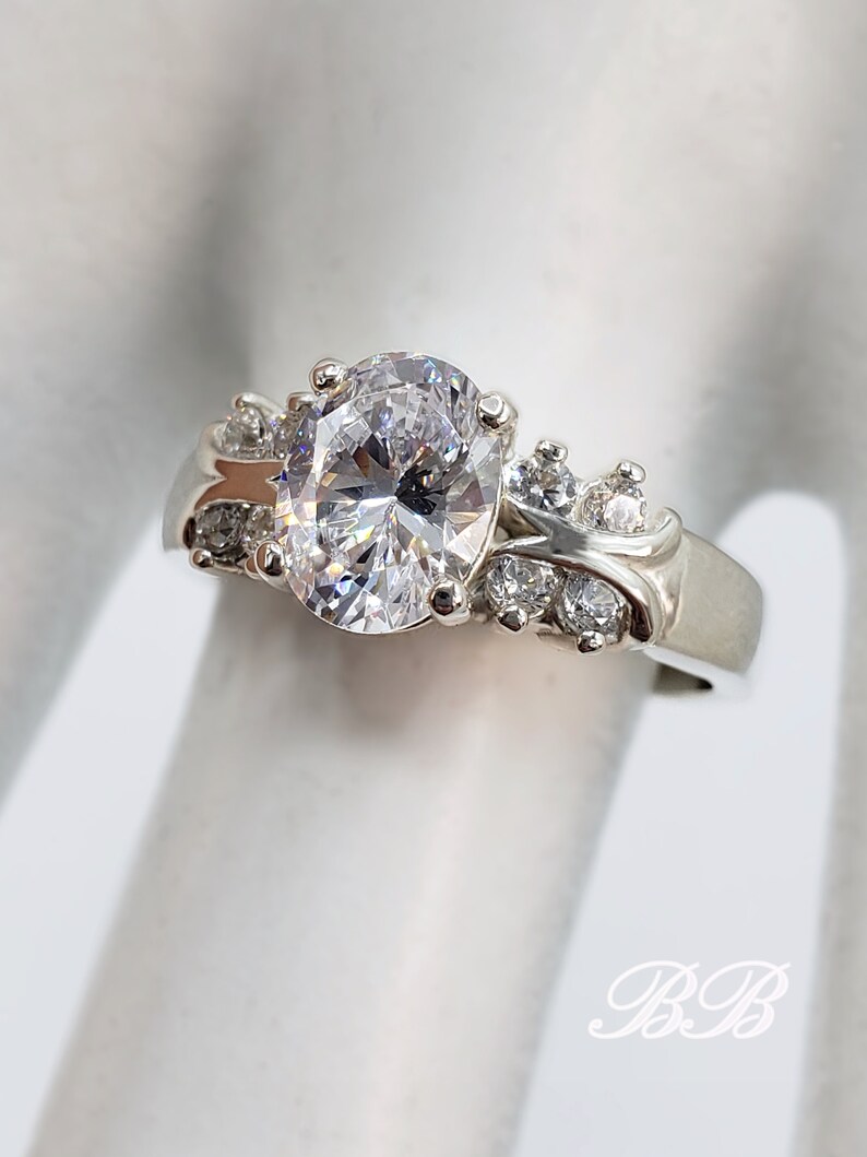 May include: A silver ring with a large oval-shaped clear stone surrounded by smaller clear stones.