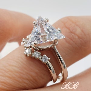 May include: A silver ring set with a large triangular-shaped clear gemstone and smaller clear gemstones on the band.