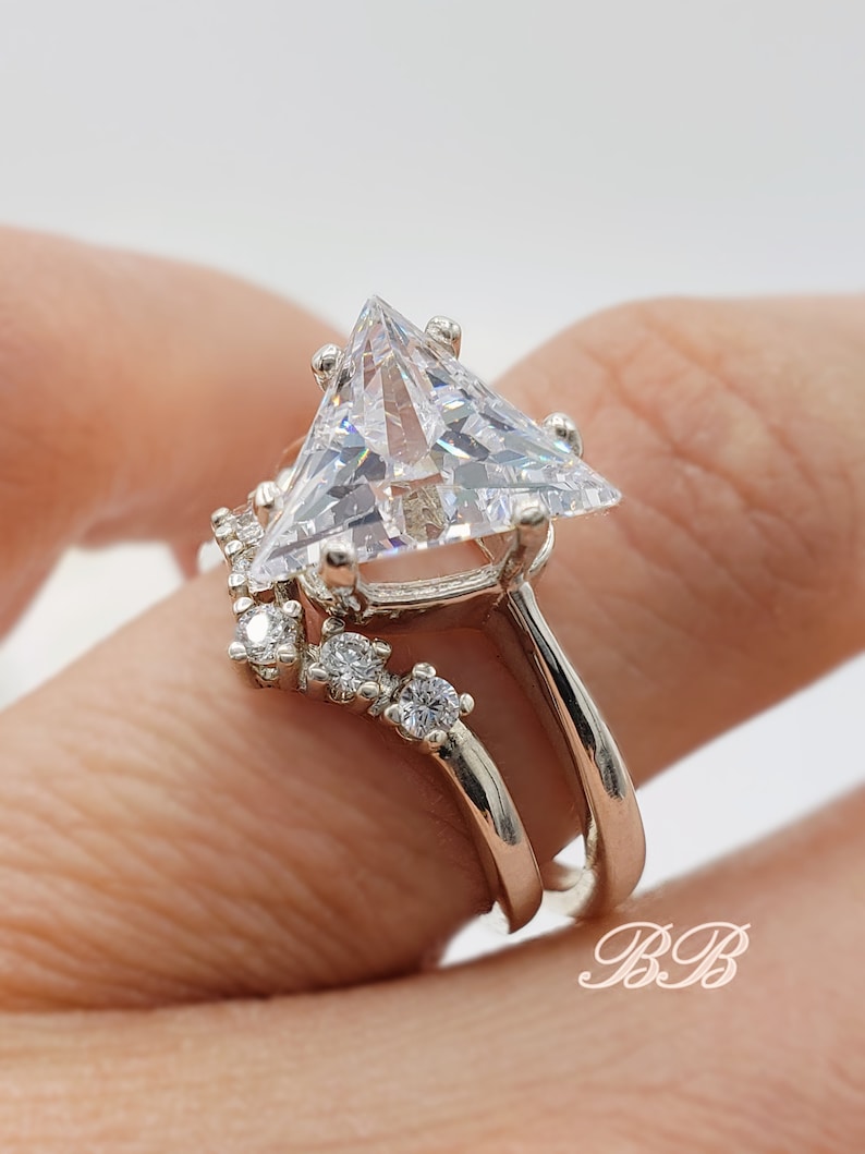 May include: A silver ring set with a large triangular-shaped clear gemstone and smaller clear gemstones on the band.