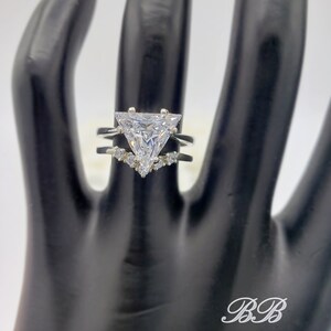May include: A silver ring with a large triangular-shaped clear stone and smaller clear stones on the band.