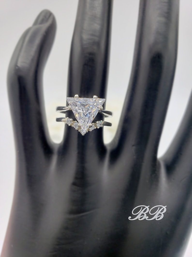 May include: A silver ring with a large triangular-shaped clear stone and smaller clear stones on the band.