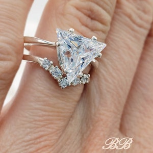 May include: A silver ring set with a large triangular-shaped clear gemstone. The ring has a delicate band with smaller clear gemstones set along the side.