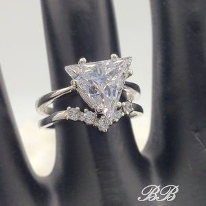 May include: A silver ring with a large triangular-shaped clear cubic zirconia stone. The ring has a smaller band with smaller clear cubic zirconia stones set in a v-shape.