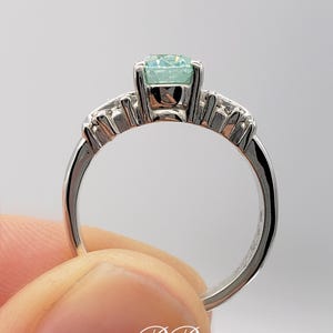 Puede incluir: Un anillo de plata con una piedra preciosa azul claro y una fila de piedras preciosas m&aacute;s peque&ntilde;as a cada lado.