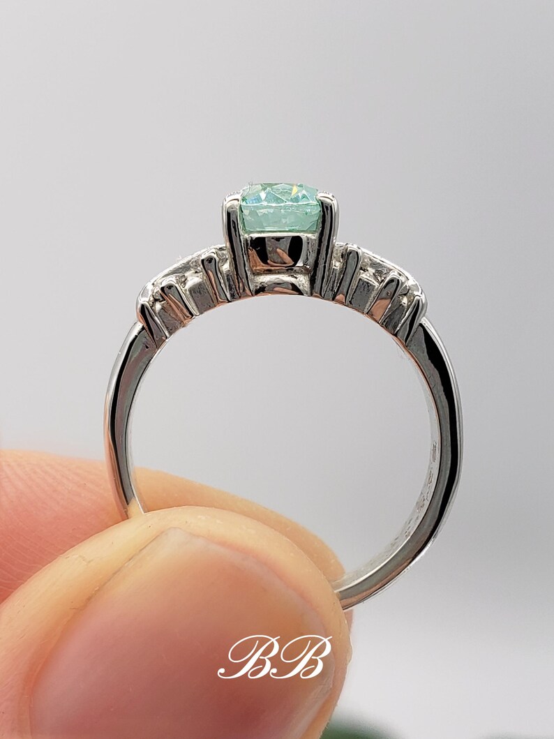 Puede incluir: Un anillo de plata con una piedra preciosa azul claro y una fila de piedras preciosas m&aacute;s peque&ntilde;as a cada lado.