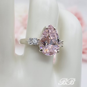 Puede incluir: Un anillo de plata con una piedra rosa en forma de pera y piedras transparentes m&aacute;s peque&ntilde;as en la banda.