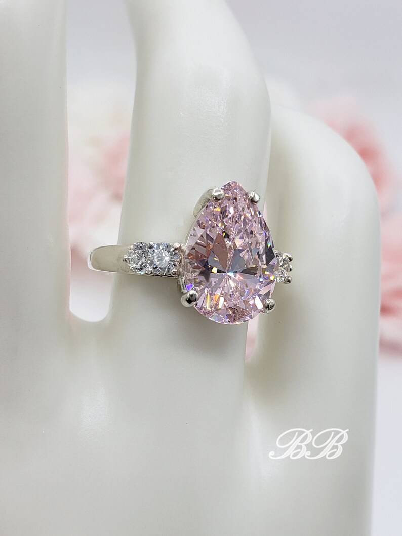 Puede incluir: Un anillo de plata con una piedra rosa en forma de pera y piedras transparentes m&aacute;s peque&ntilde;as en la banda.