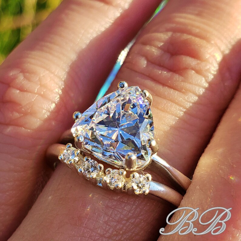 May include: A silver ring set with a large, clear, triangular-shaped gemstone. The ring is accented with smaller, clear gemstones on the band.