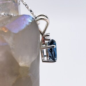 May include: A silver pendant necklace with a dark blue gemstone set in a cage-like design. The gemstone is surrounded by smaller clear gemstones.
