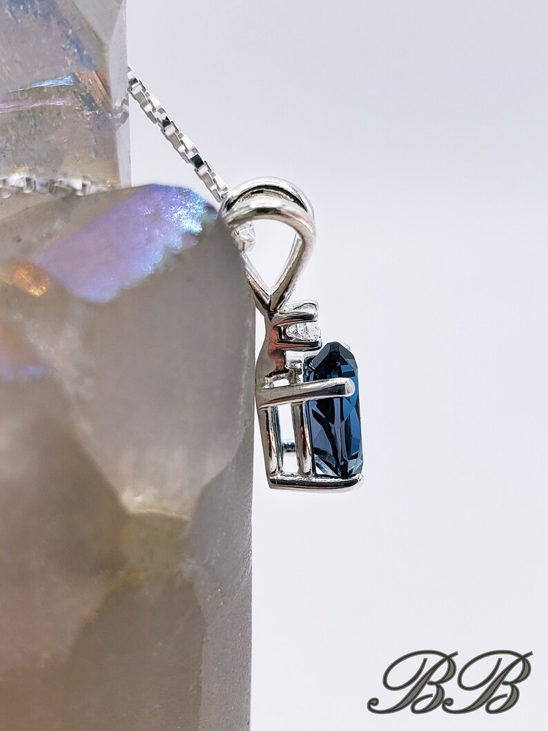 May include: A silver pendant necklace with a dark blue gemstone set in a cage-like design. The gemstone is surrounded by smaller clear gemstones.