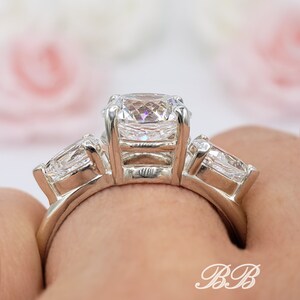 May include: A silver ring with three clear cubic zirconia stones. The center stone is a square cut, and the two side stones are pear shaped.