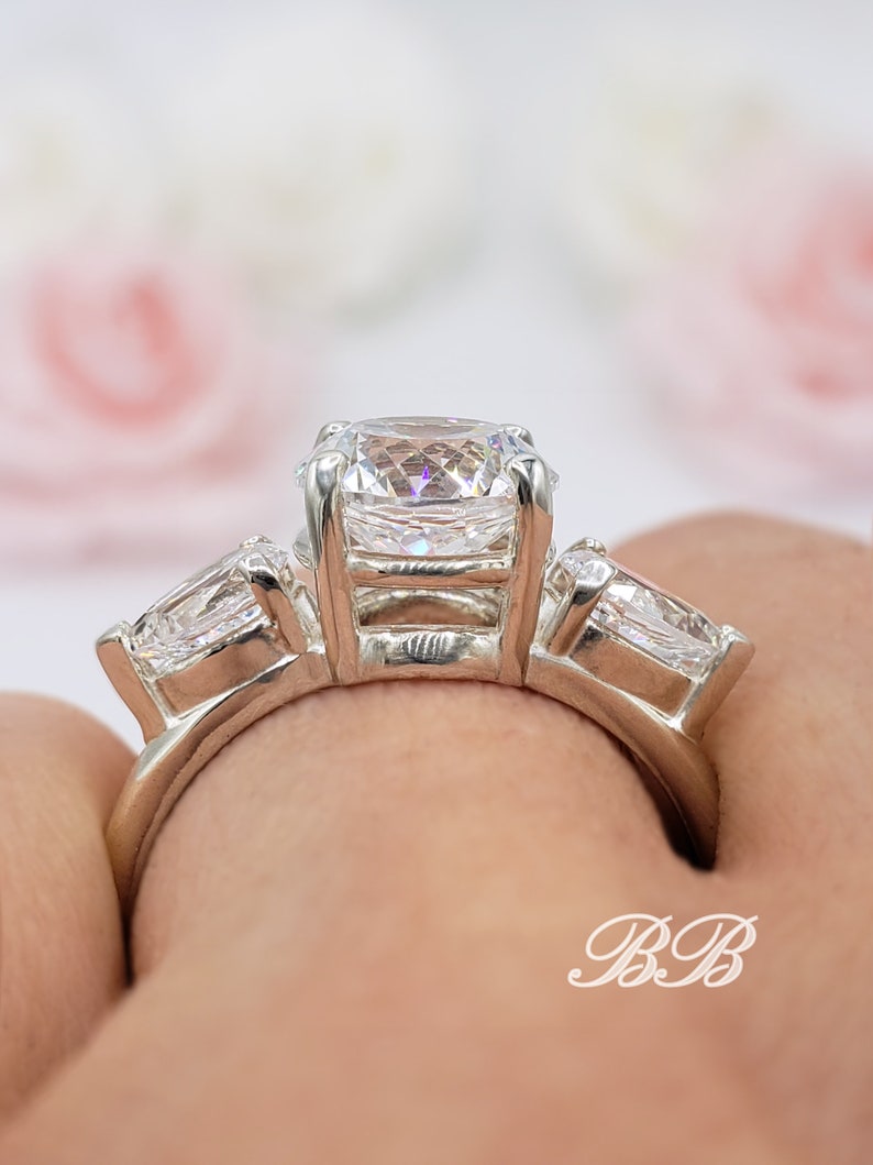 May include: A silver ring with three clear cubic zirconia stones. The center stone is a square cut, and the two side stones are pear shaped.