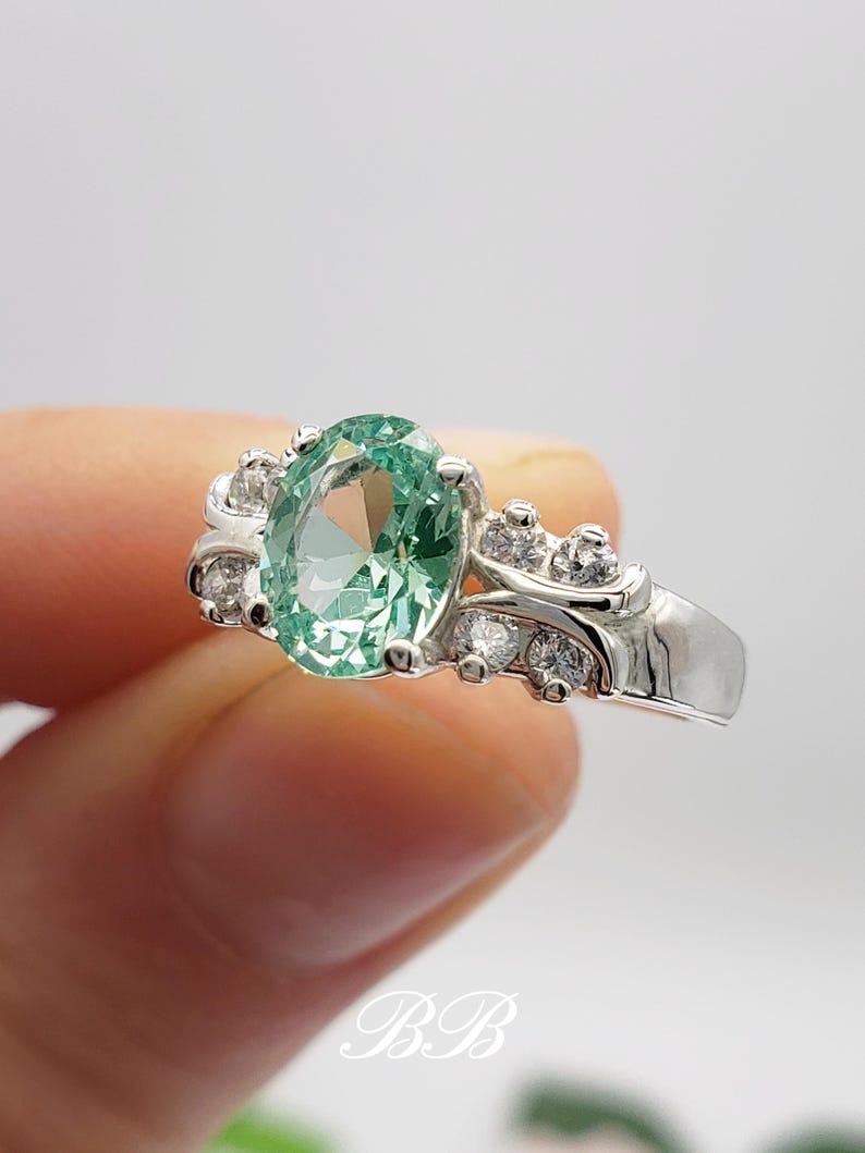 May include: A silver ring with a large oval green gemstone surrounded by smaller clear gemstones.