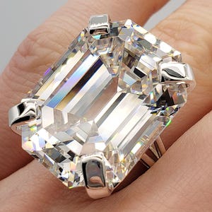 Puede incluir: Un anillo de plata con una gran piedra preciosa transparente de talla esmeralda. El anillo está en un dedo.