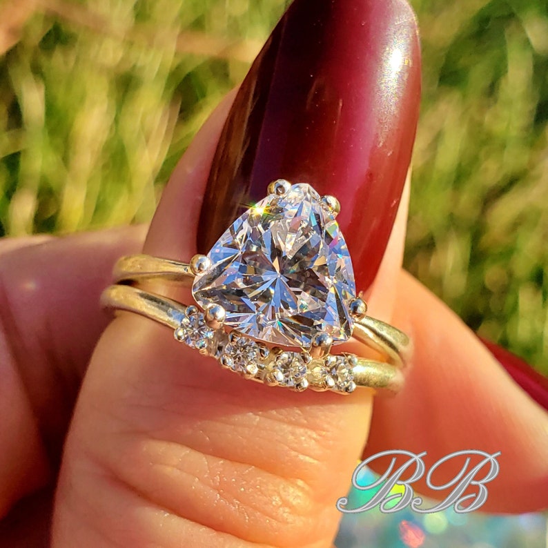 May include: A silver ring with a large triangular-shaped clear gemstone. The ring is set with smaller clear gemstones around the main stone.