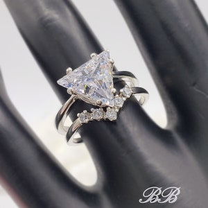 May include: A silver ring with a large triangular-shaped clear stone and smaller clear stones set in a v-shape on the band.