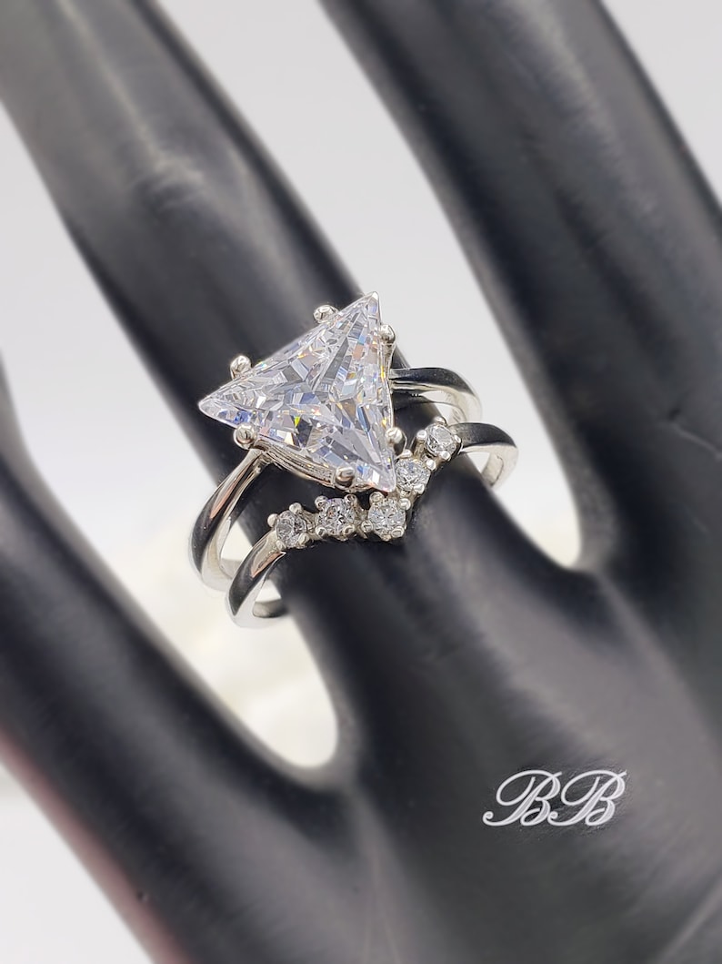 May include: A silver ring with a large triangular-shaped clear stone and smaller clear stones set in a v-shape on the band.