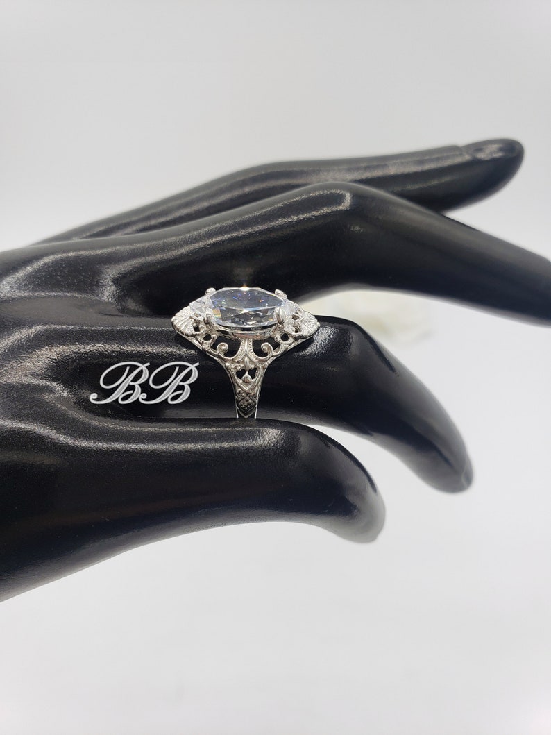 Puede incluir: Un anillo de plata con una gran piedra ovalada transparente engastada en un dise&ntilde;o de filigrana.