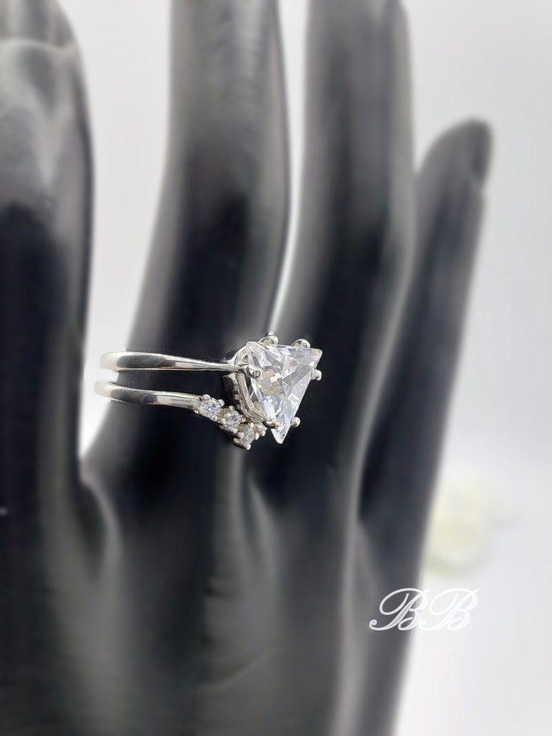 May include: A silver ring with a large triangular-shaped clear stone and smaller clear stones on the band.
