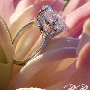 May include: A silver ring with a large, clear, round-cut gemstone set in a prong setting. The ring is on a pink flower.
