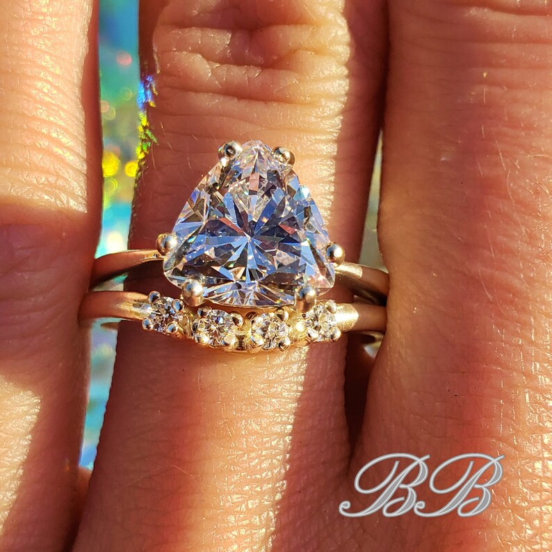 May include: A gold ring set with a large, clear, triangular-shaped gemstone. The ring is accented with smaller, clear gemstones on the band.