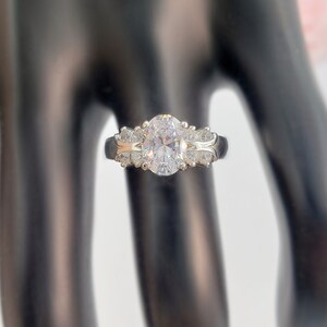 May include: A silver ring with a large oval-shaped clear stone surrounded by smaller clear stones.