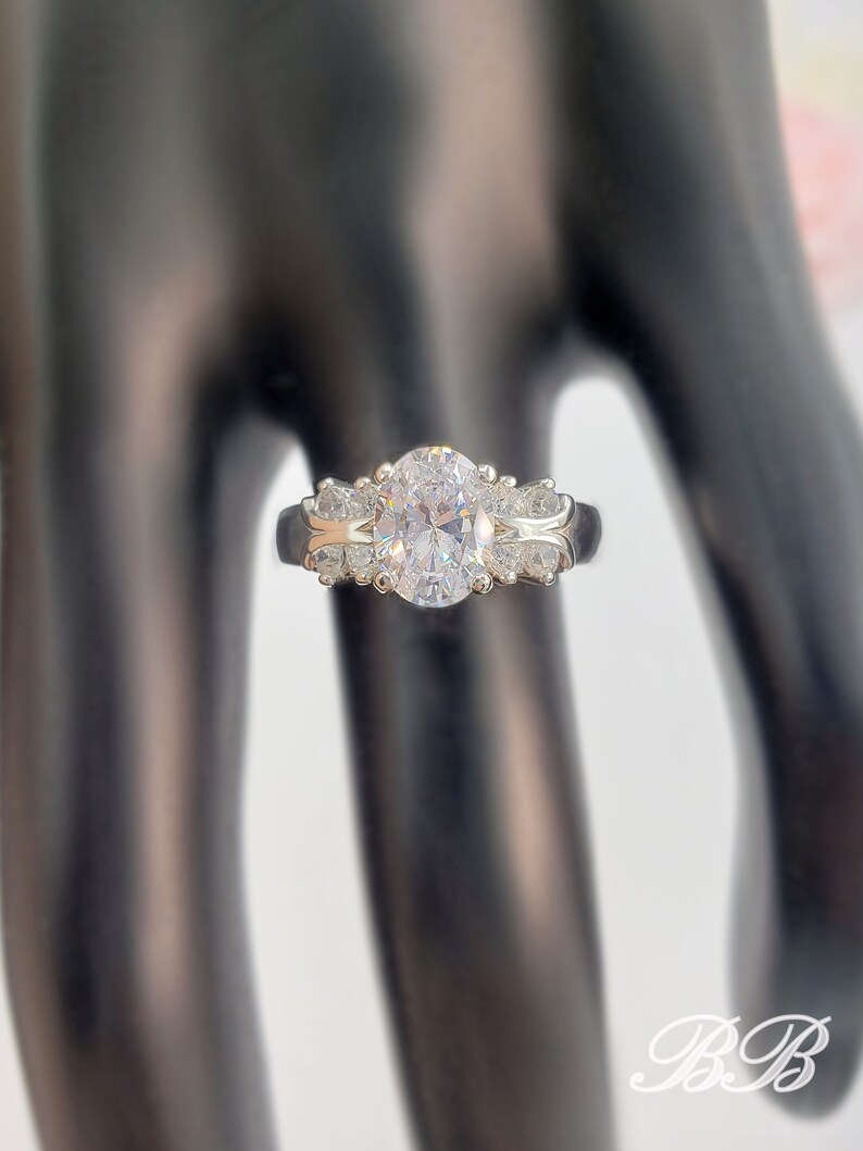 May include: A silver ring with a large oval-shaped clear stone surrounded by smaller clear stones.