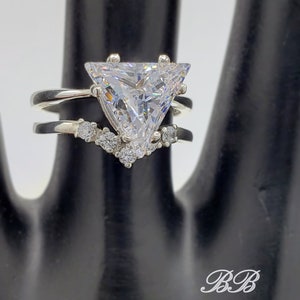 May include: A silver ring set with a large triangular-shaped clear stone and smaller clear stones on the band.